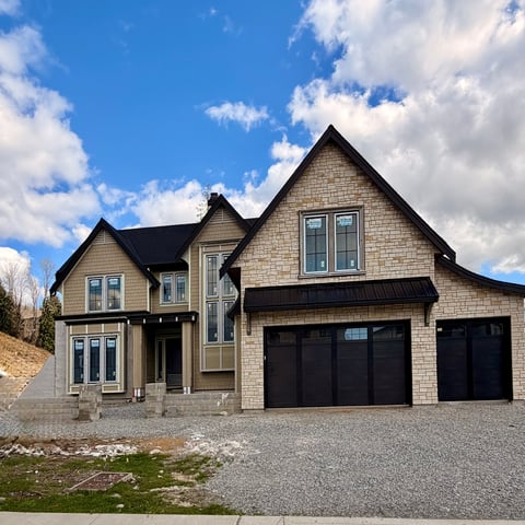 Modern two-story stone and brick house with dark roof and black garage doors on a sunny day with blue sky