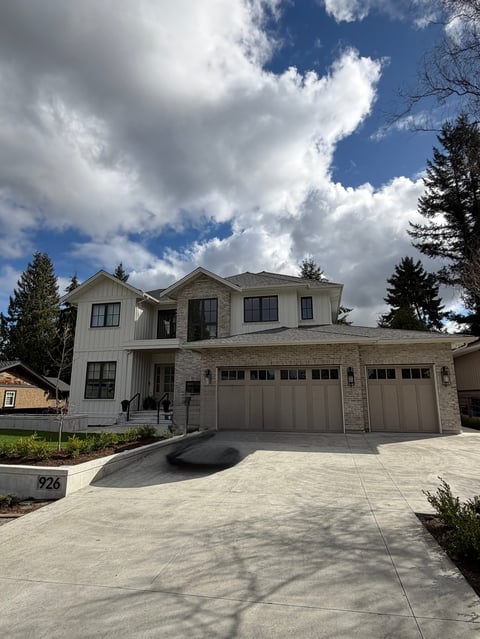 Modern two-story suburban house with stone and white facade, three-car garage, and manicured landscaping